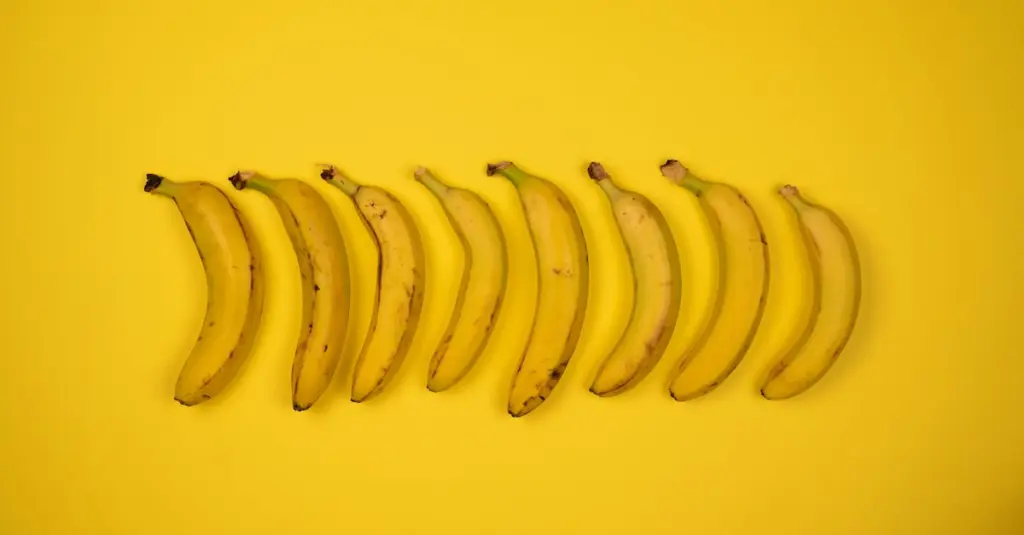 Top view of tasty ripe bananas with blots on peel composed in row on yellow background